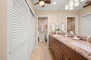 A bathroom with a double sink, vanity, and a ceiling fan.