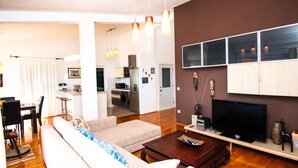 Ein modernes Wohnzimmer mit einer Couch, einem Couchtisch, einem Fernseher und einer Küche im Hintergrund.