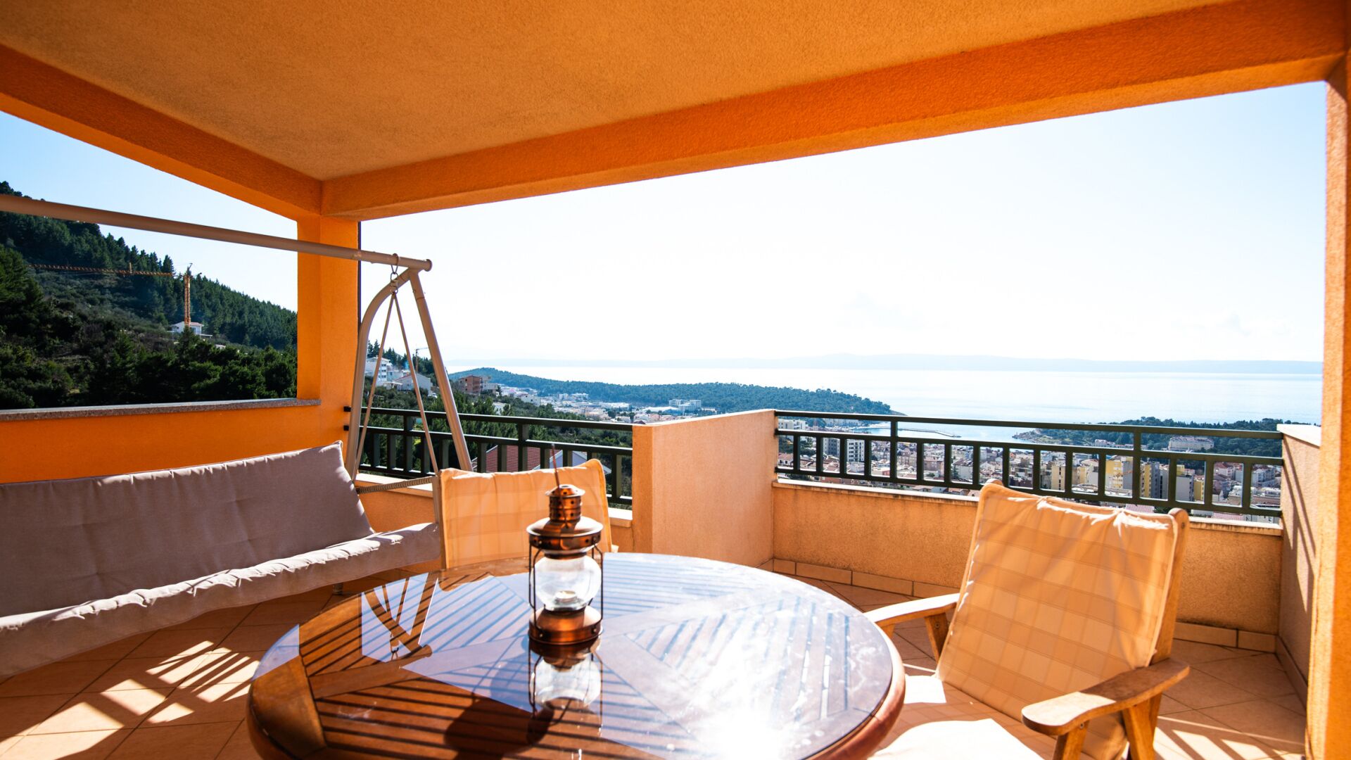 A balcony with a round table, two chairs, and a hanging swing.