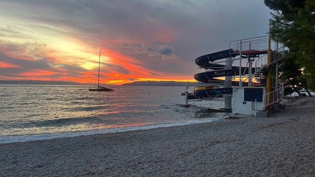 Eine Küstenlandschaft mit Sonnenuntergang, einem Segelboot und einem mehrstöckigen Steg mit Booten.