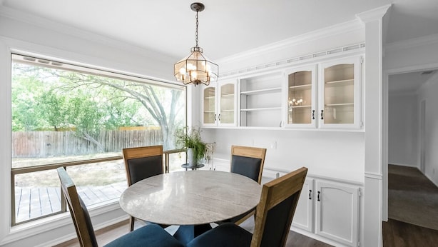 A dining area with a round table, six chairs, a chandelier, and built-in white cabinets with glass doors. - 12 Mins to airport (San Antonio)