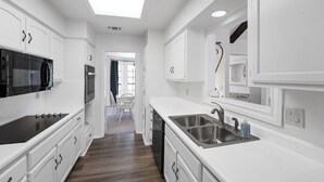 A modern kitchen with white cabinetry, stainless steel appliances, and a central island with a sink. - 12 Mins to airport (San Antonio)