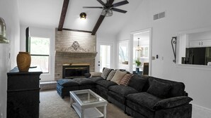 A living room with a sectional sofa, a glass coffee table, a fireplace, and a ceiling fan. - 12 Mins to airport (San Antonio)