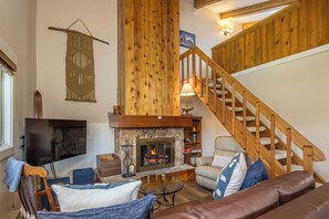 A cozy living room with a fireplace, wooden staircase, and a flat-screen TV.