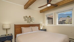 Ein Schlafzimmer mit einem großen Bett, Holzbalken an der Decke, einem Deckenventilator und einem Fenster mit Blick auf die Berge.