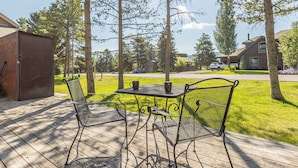 Eine Terrasse mit Metallstühlen und einem Tisch, mit Blick auf eine grüne Wiese und Häuser.
