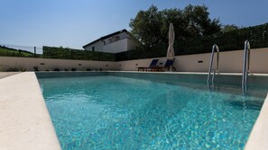A swimming pool with clear blue water, a lounge chair, and a sun umbrella. - Villa Olea by Villas Guide (Blace)
