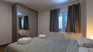 A bedroom with a bed, a mirror, a window with curtains, and a bedside table with a lamp.