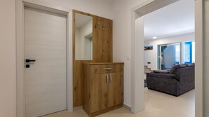 Een gang met een houten garderobe, een witte deur en een grijze bank op de achtergrond.