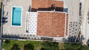 An aerial view of a resort with a swimming pool, sun loungers, and a covered patio area.