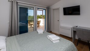 A hotel room with a bed, a desk, a chair, a TV, and a balcony with chairs. - Villa Olea by Villas Guide (Blace)