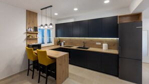 A modern kitchen with black cabinets, a wooden countertop, and a built-in dishwasher. There are two yellow chairs at a wooden table.