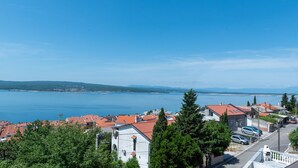 Eine Küstenstadt mit roten Dächern, blauem Meer und Bergen im Hintergrund.