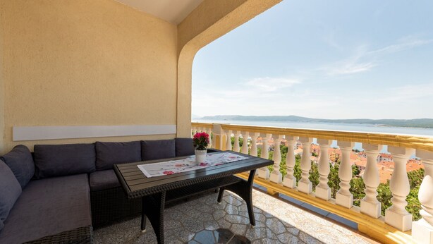 Ein Balkon mit einer Couch und einem Tisch, mit Blick auf die Küste.