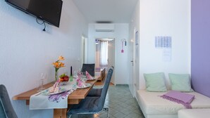 Ein Essbereich mit einem Tisch für vier Personen, Stühlen, einer Couch und einem an der Wand montierten Fernseher.