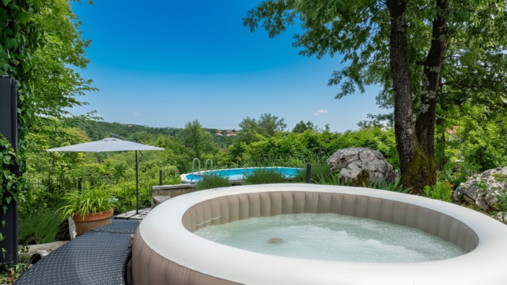 Een hottub omringd door begroeiing, een zwembad en een heldere lucht.