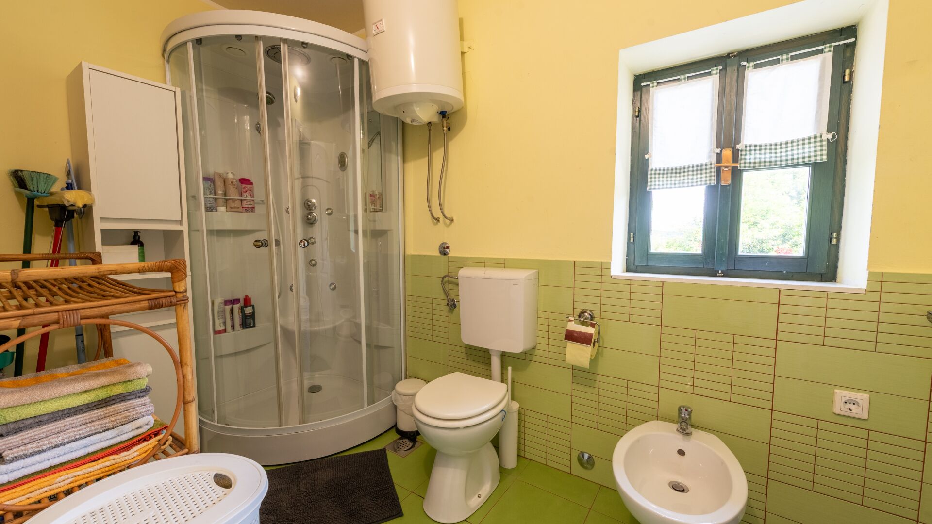 A bathroom with a shower, toilet, bidet, and a window.