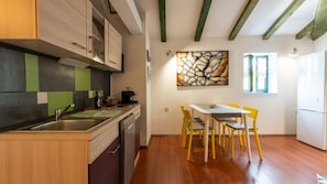 Une cuisine avec des meubles en bois, un coin repas avec des chaises jaunes, un réfrigérateur et une œuvre d’art murale en pierre.
