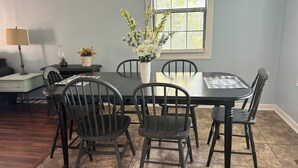Un comedor con una mesa redonda, cuatro sillas, un florero con flores, una lámpara y una pequeña mesa con una planta.
