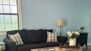 Una sala de estar con un sofá de color oscuro, una mesa de centro de madera y una lámpara.