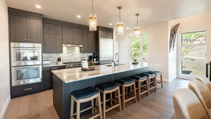 Una cocina moderna con gabinetes oscuros, electrodomésticos de acero inoxidable, una isla de mármol y taburetes de bar.