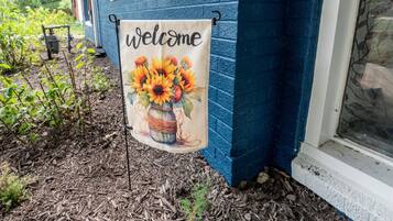 A welcome banner with sunflowers and a basket, hanging on a blue house exterior.