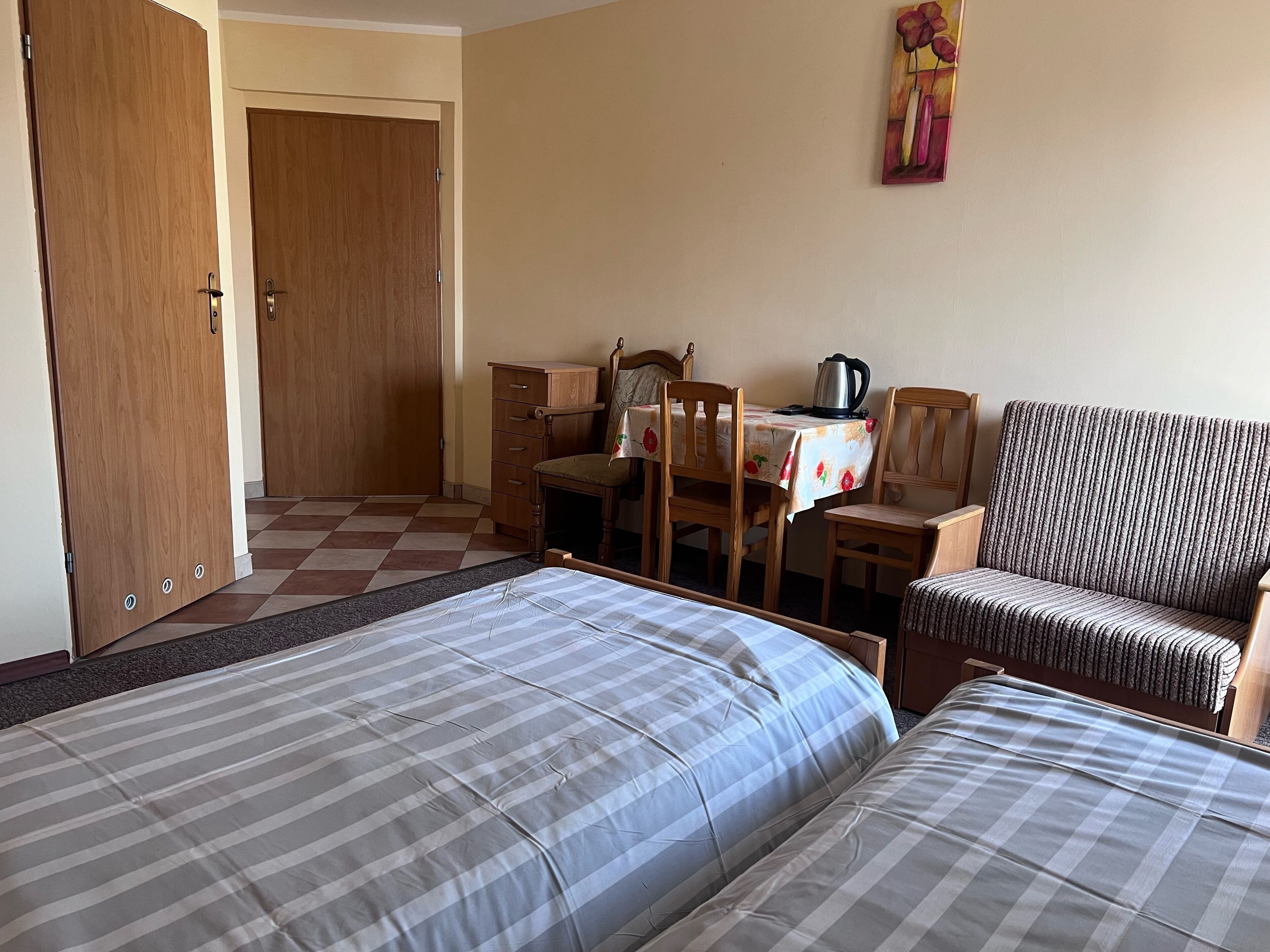 Ein Hotelzimmer mit zwei Betten, einem Holztisch, einem Stuhl und einem Tisch mit Blumenmuster.