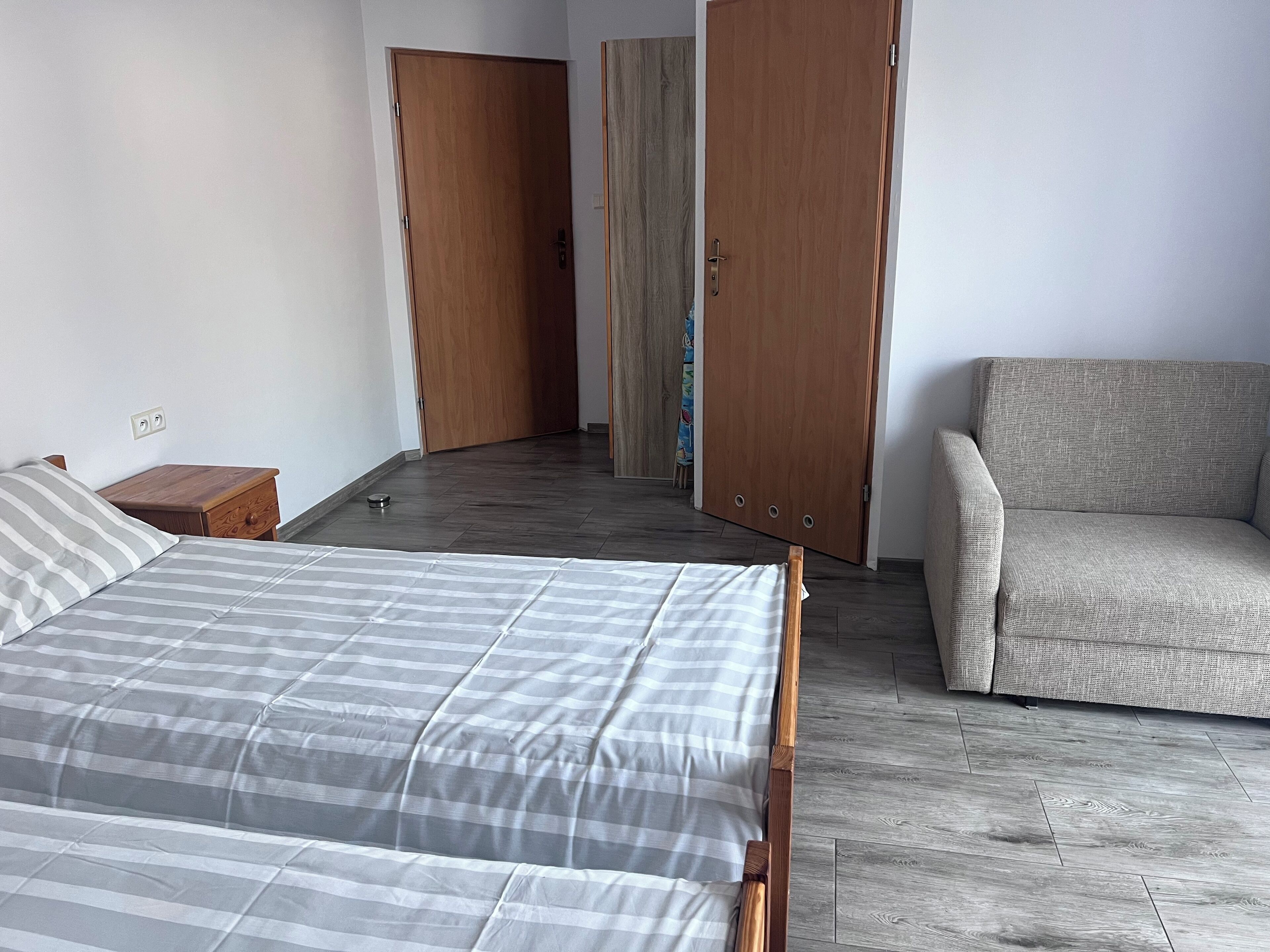 A bedroom with a bed, a wooden nightstand, a sofa, and two wooden doors.