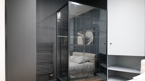 Une chambre moderne dotée d’un dressing fermé par des parois de verre, d’un lit avec une tête de lit blanche et d’une bibliothèque intégrée.
