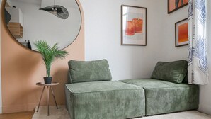 Un canapé vert, un miroir rond et une petite plante en pot, le tout placé dans un coin.