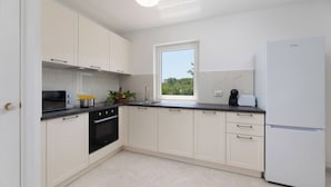 A modern kitchen with white cabinets, a black stove, and a white refrigerator. - Villa Stjepan Zep (Kvarner - Županje) (Županje)
