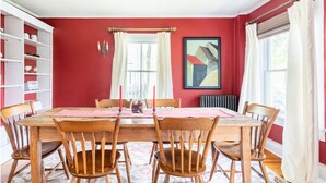 Ein Esszimmer mit Holztisch und -stühlen, roten Wänden und einem Bücherregal.