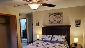 Ein Schlafzimmer mit einem Bett, zwei Nachttischlampen, einem Deckenventilator und einer Weltkarte als Wandbild.