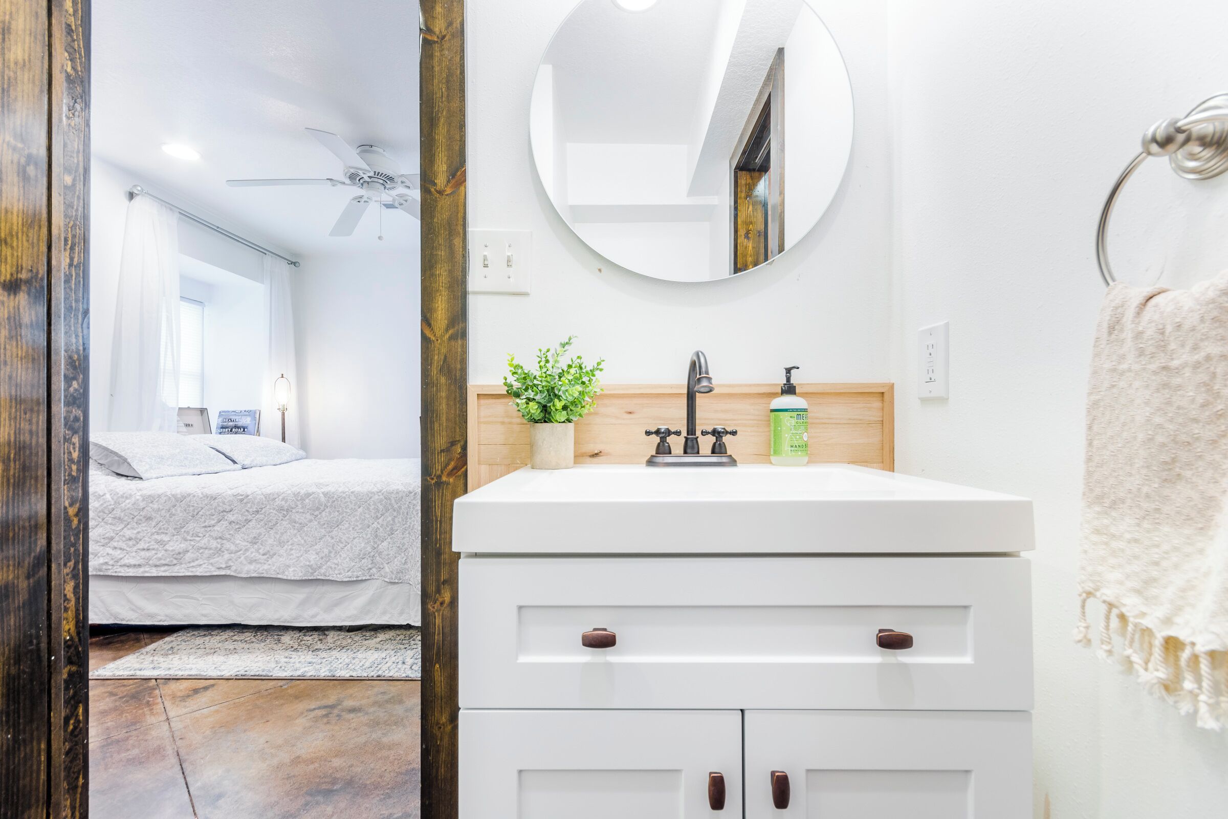 A modern bathroom with a white vanity, a round mirror, a small plant, and a towel rack.