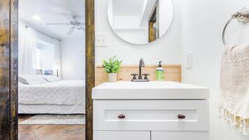 A modern bathroom with a white vanity, a round mirror, a small plant, and a towel rack.