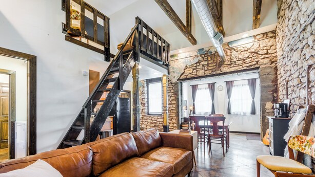 Un vaste espace de vie comprenant un canapé en cuir, un escalier, des murs en pierre et un coin repas.