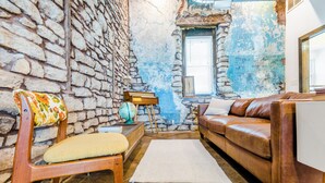 Un salon chaleureux avec un mur en pierre, un canapé en cuir marron, une chaise en bois avec un coussin et un tapis blanc.