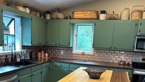 Una cocina con gabinetes verde azulado, una isla de madera y un salpicadero de ladrillo.