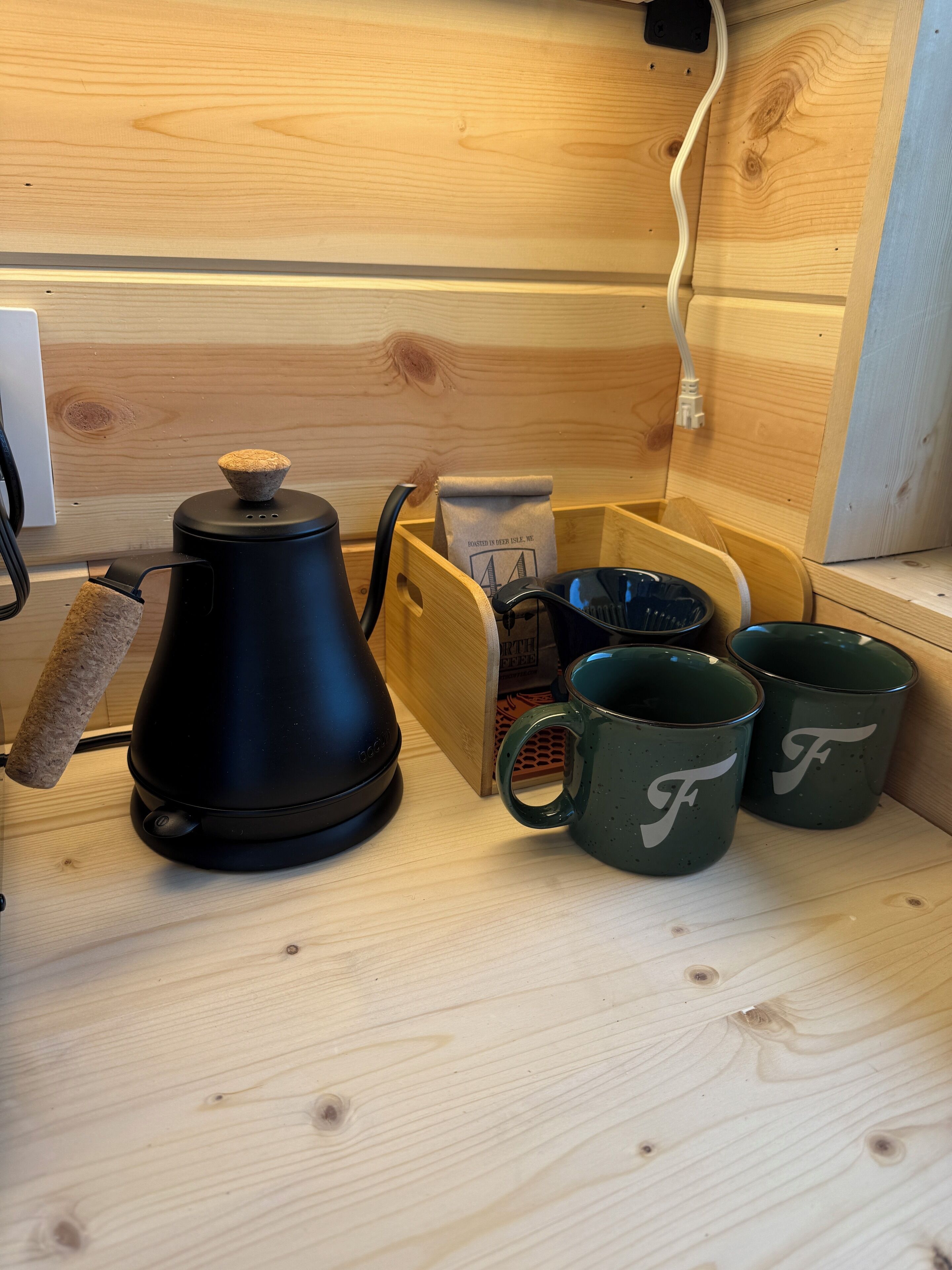 Una cafetera, un molinillo, un paquete de café y dos tazas sobre una superficie de madera.