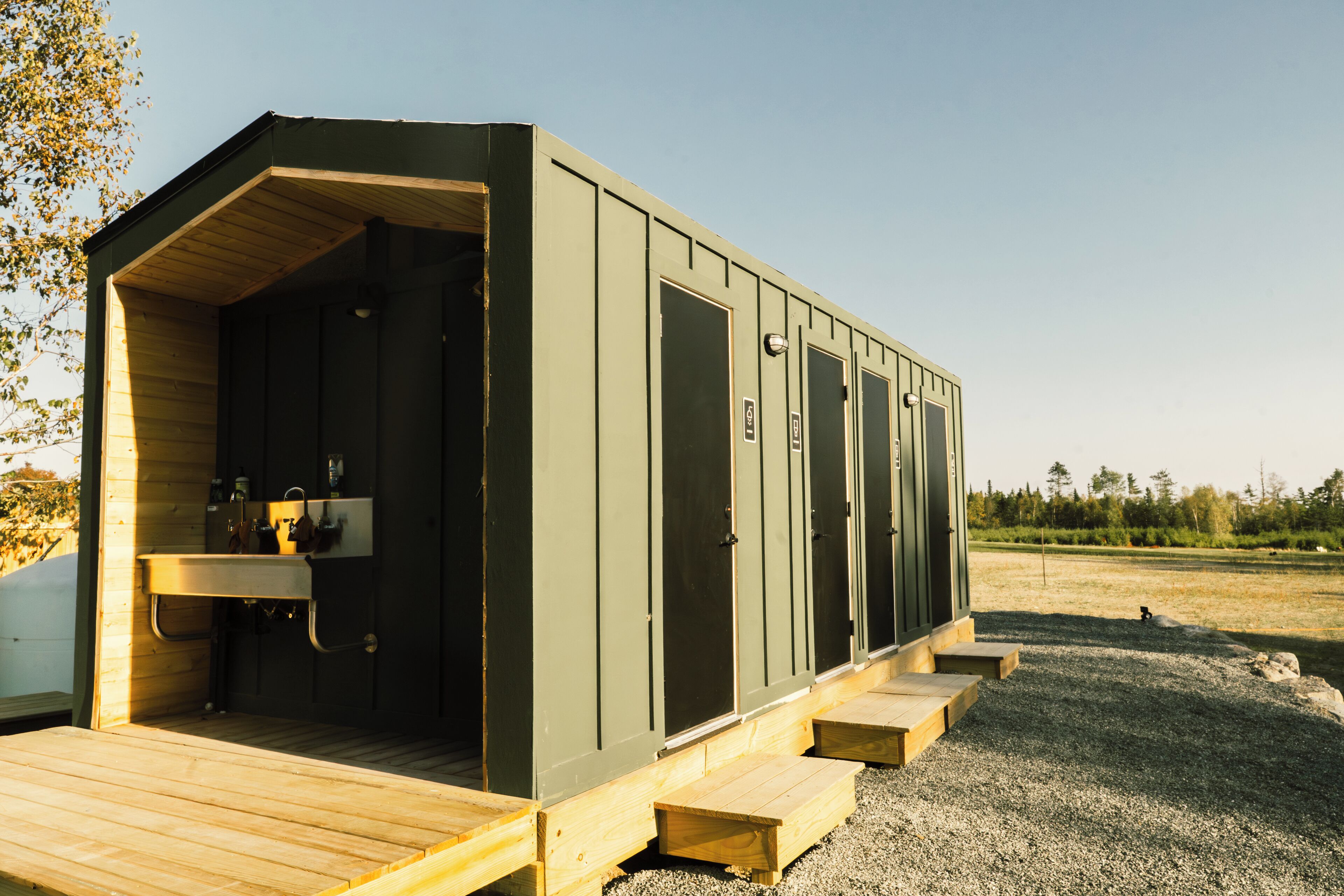 A portable outdoor bathroom with a wooden deck, a sink, and multiple doors.