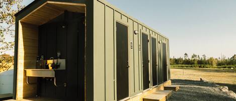 A portable outdoor bathroom with a wooden deck, a sink, and multiple doors.