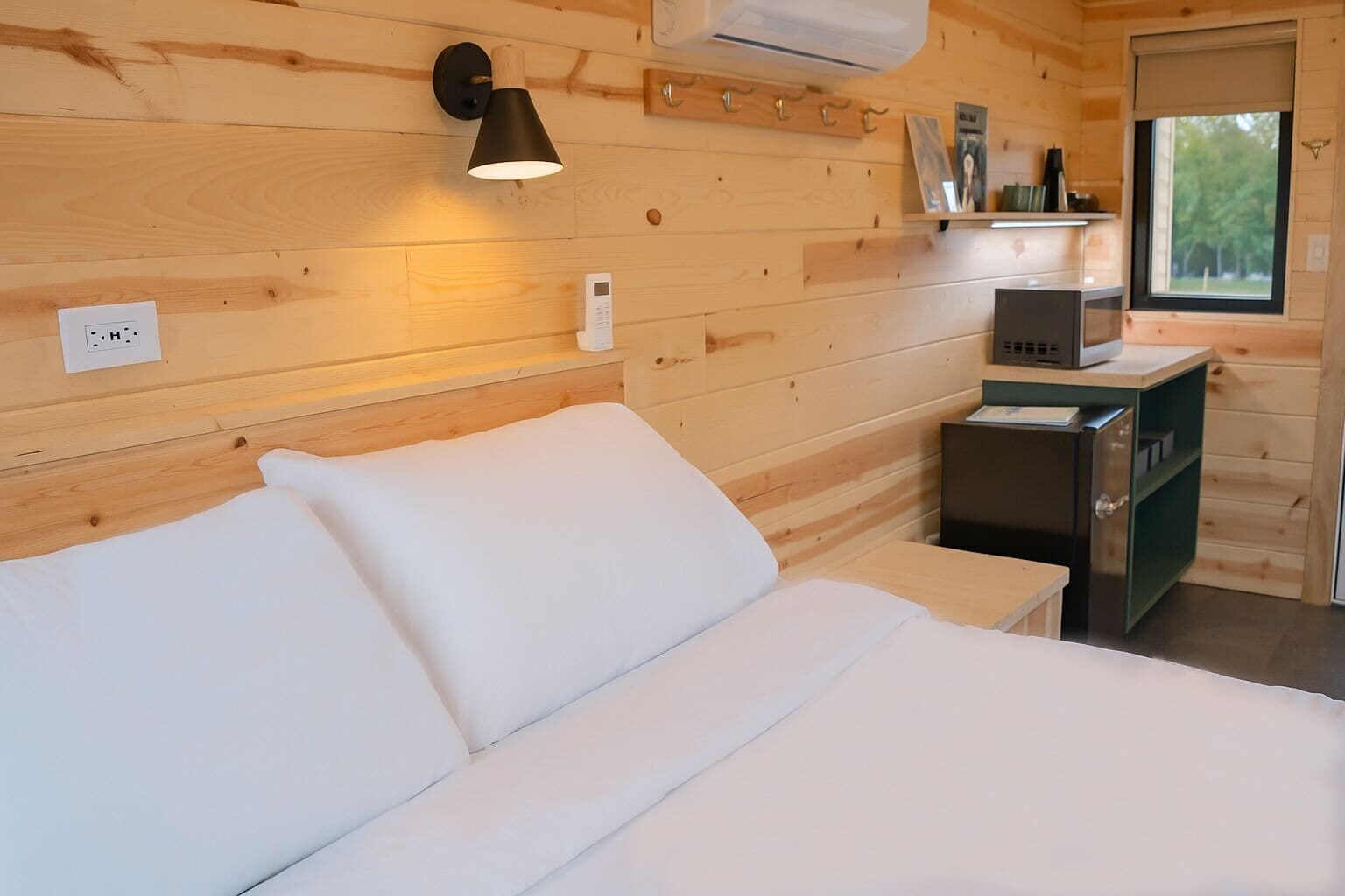 Een knus houten kamer met een bed, een nachtkastje, een lamp en een raam.