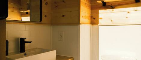 A bathroom with a wooden interior, a white sink with a black faucet, a mirror above the sink, and a toilet visible to the right.