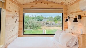 A wooden cabin bedroom with a bed, a window, and a view of greenery outside. - Ferncrest Acadia (Sedgwick)