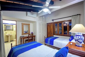 Ein Hotelzimmer mit zwei Betten, einem Holztisch, einem Spiegel und einem Deckenventilator.
