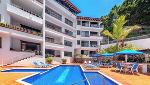 A hotel with a swimming pool, multiple balconies, and outdoor seating areas.
