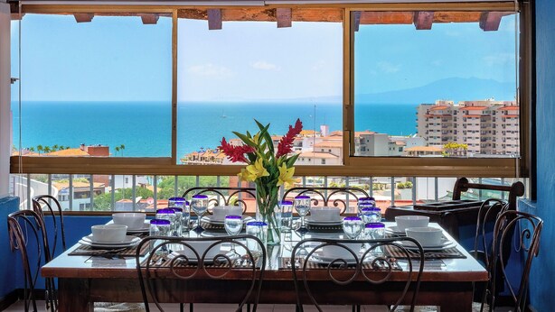 A dining table set for four with a view of the sea and buildings in the background.