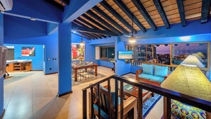 A spacious living area with a high ceiling, a dining area, and a view of the cityscape through large windows.