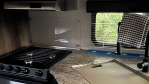 A compact kitchen with a stove, a window with blinds, and a countertop. - Quaint RV with AC can be picked up in Berrien Springs 29ft a slide out also. (Berrien Springs)