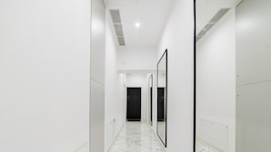 A corridor with white walls, a marble floor, and framed mirrors on one side.